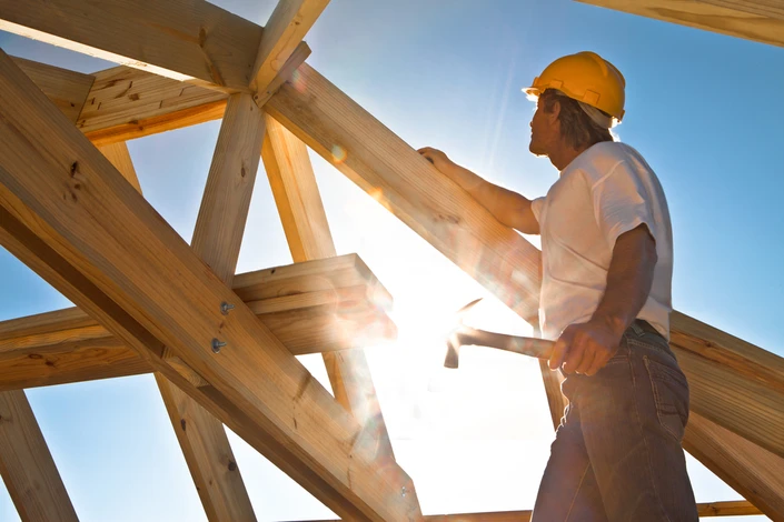 Chantier de construction extérieur, charpentier en casque jaune travaillant sur une structure en bois