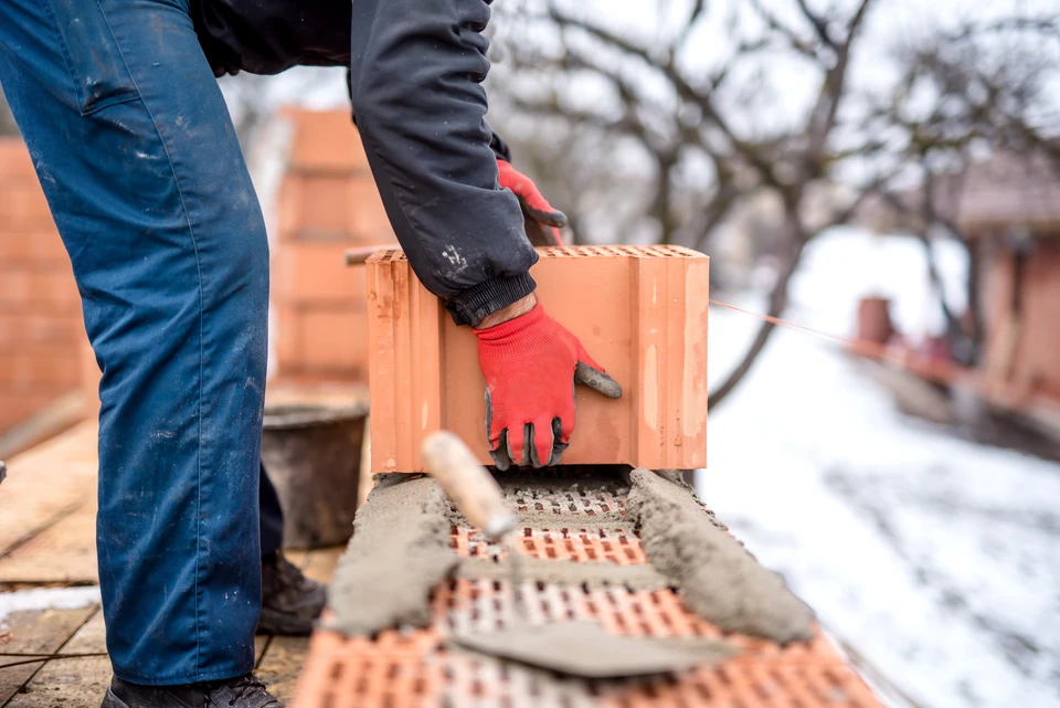Chantier de construction extérieur avec ouvrier plaçant brique perforée rouge sur mur en cours d'édification