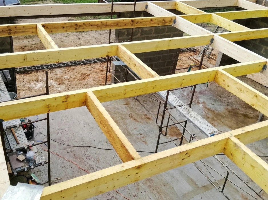 Construction d'une maison à ossature bois en cours, charpente traditionnelle apparente avec poutres et chevrons en bois naturel