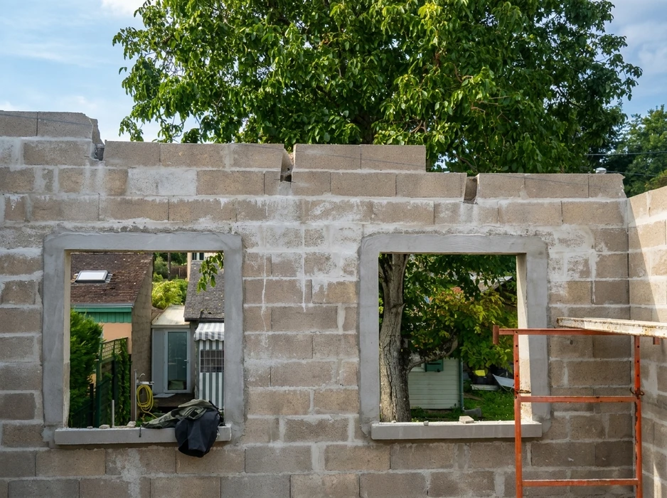Chantier de construction résidentielle en extérieur avec dalle béton fraîchement coulée et structure bois en cours d'érection