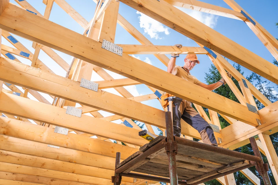 Chantier de construction extérieur avec trois ouvriers installant la charpente d'une toiture